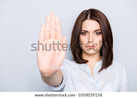 Portrait of stylish, charming, pretty, modern, caucasian, brunette, concentrated, thoughtful woman in shirt gesturing palm front, stop sign to the camera, isolated on grey background Royalty-Free Stock Photo #1050039158