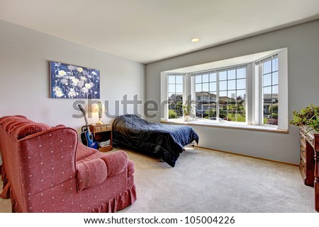 Bedroom with large window and small bed with armchair and art.