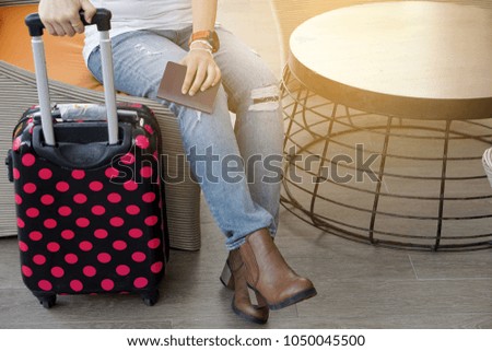 Woman wears torn jeans holds pink polka dot luggage and passport sitting in the airport waiting for the flight