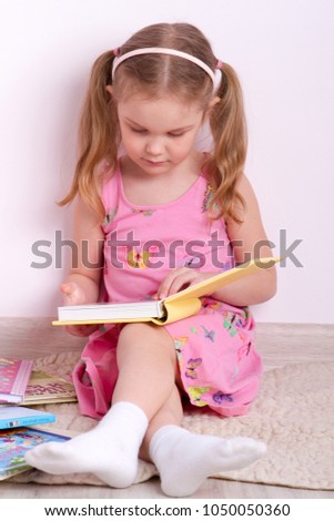 little girl is sitting near the wall and is reading a book