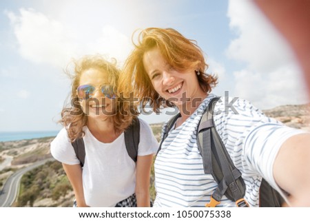 two attractive young girls travel together, do selfie on the phone against the sky and landscape in the mountains in the sun