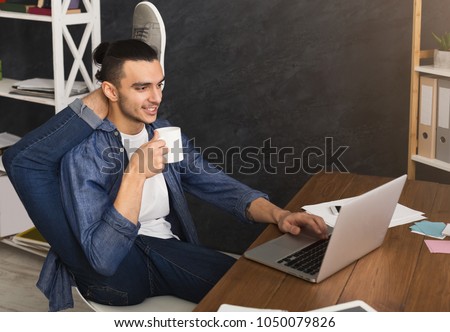 Short break for yoga in office. Flexible man practicing yoga at workplace, while typing on laptop and having coffee, copy space. Active employee at work, healthy lifestyle concept Royalty-Free Stock Photo #1050079826