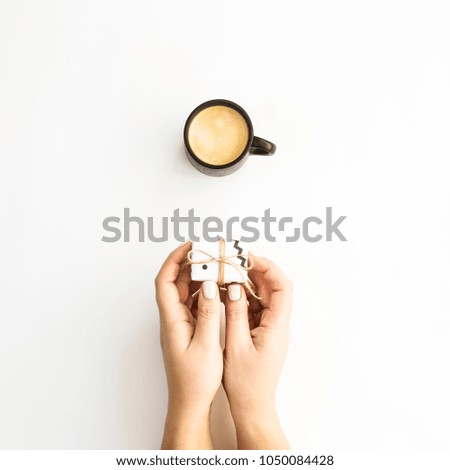 Female hands holding a small minimalist gift near a cup of coffee on a white background. Flat lay, top view