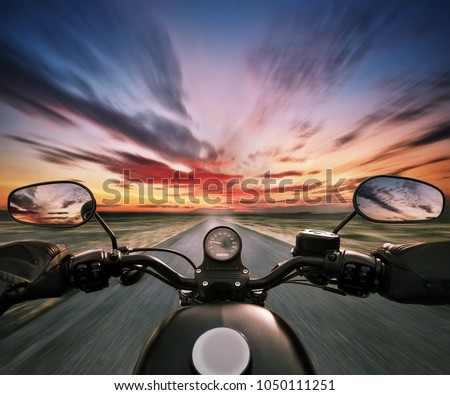 POV of motorbiker holding steering bar in beautiful sunset dramatic sky. Travel and freedom, outdoor activities. Motion blur
