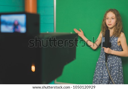 Little girl with microphone standing in front of camera on green screen.