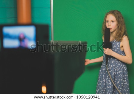 Little girl with microphone standing in front of camera on green screen.