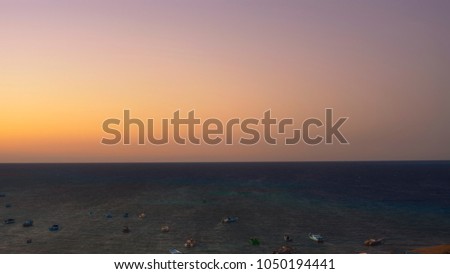 ships standing on anchor in the foreground orange sky and blue ocean in the background coloured warm colours