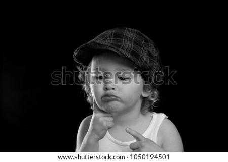 A black and white portrait of a little boy wearing a white tank top thinking and daydreaming.  He may have an idea or is wondering. There is room for text or words with a solid black background. 