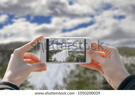 Girl holding phone and taking photo of nature ski track with two hands