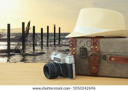 traveler vintage luggage, camera and fedora hat over wooden table infront of sunset landscape. holiday and vacation concept.