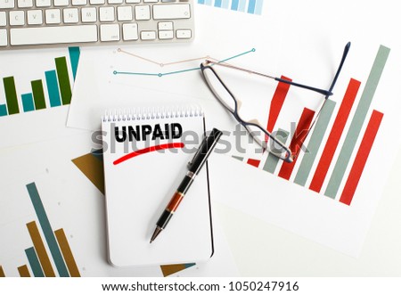 Conceptual background with the word Unpaid written in the notebook that is next to economy, keyboard, ballpoint and fas charts. Concept.