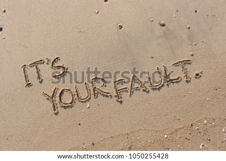Handwriting  words "IT'S YOUR FAULT." on sand of beach. Royalty-Free Stock Photo #1050255428