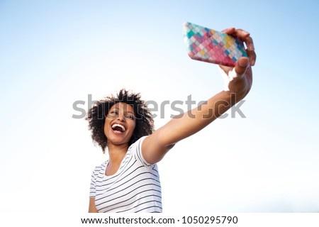 Portrait of laughing young african american woman taking selfie with smart phone outdoors