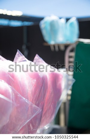 Close up on bags of pink cotton candy, with blue sugar floss in the background, at a stadium concession stand