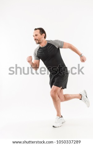Photo in profile of content energetic sportsman 30s wearing shorts and t-shirt smiling and running marathon or doing workout isolated over white background