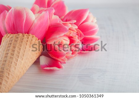 Flatlay waffle sweet ice cream cone with pink tulips blossom flowers over white wood background, top view. Spring or summer mood concept.