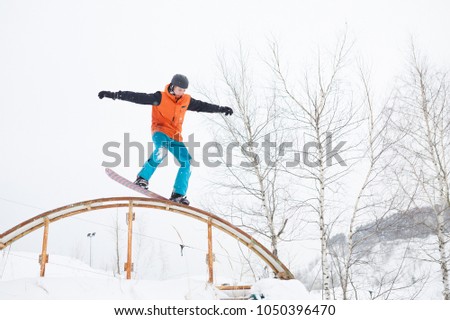 Image of young sportive man skiing on snowboard with springboard against background of trees