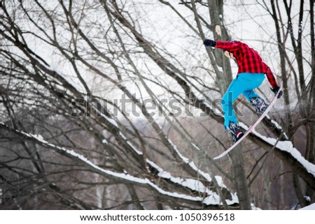 Image of sportive man wearing helmet jumping on snowboard against background of winter trees