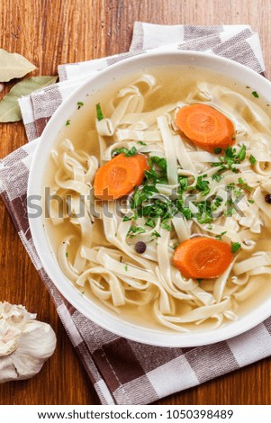 Tasty meat broth with noodles, carror and parsley in a plate. Top view