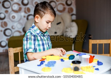 Picture of a boy playing with color play dough and cutters. Having fun with colorful modeling clay. Creative kids molding at home. Children play with plasticine or dough. 