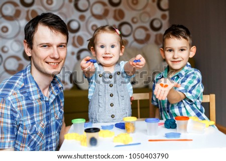 Picture of a father, daughter and son playing with color play dough and cutters. Having fun with colorful modeling clay. Creative kids molding at home. Children play with plasticine or dough.