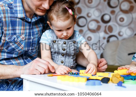 Picture of a father and daughter playing with color play dough and cutters. Having fun with colorful modeling clay. Creative kids molding at home. Children play with plasticine or dough.
