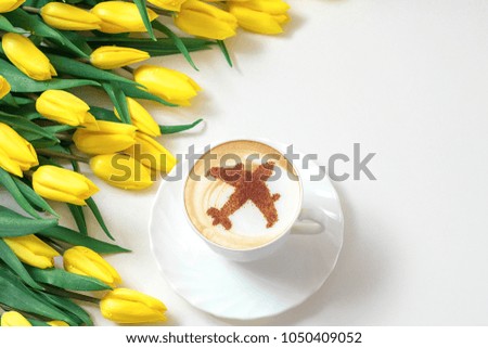 cappuccino in a white cup with a picture of an airplane and a bouquet of yellow tulips