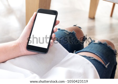 Mockup image of woman's hand holding black mobile phone with blank white desktop screen in cafe