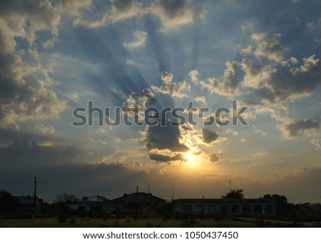 In the picture sunrise .Beautiful sky with sun rays through trees, birds in the sky, clouds and village houses.