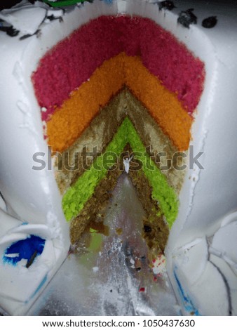 Close up of layered cake with rainbow colors on a silver plate, white and blue icing background.