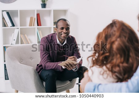 Smiling african american psychiatrist talking to young couple Royalty-Free Stock Photo #1050440903