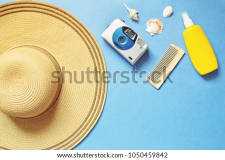 Flat lay photo sun hat, vintage camera, wooden comb, yellow sunscreen bottle and seashells on a blue background. Women's accessories for for beach holidays
