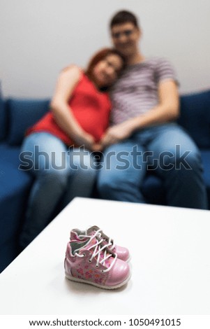 Blurry pose of a pair of pink baby girl's shoes with pregnant parents in the background. Focus on the pink shoes.