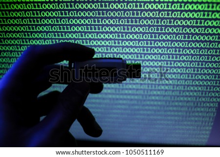USB flash drive on a background of green binary code. Image of binary code, green numbers on a black background. A man holds a USB flash drive on the background of a computer monitor