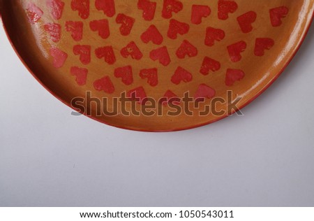 Close-up half handmade ceramic plate with heart print on the white background. A gift for St. Valentine's Day. Pottery design. 