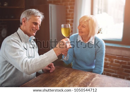 Interesting picture of an old man sitting at the table with his wife and holding a bocal of wine. They are celebrating an anniversary of their marriage.