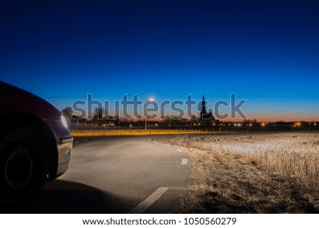 Car front beside highway with background of church and buildings.