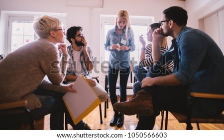Young people with problems listening to their nervous female friend confession with shock reaction while sitting together on special group therapy. Royalty-Free Stock Photo #1050566603
