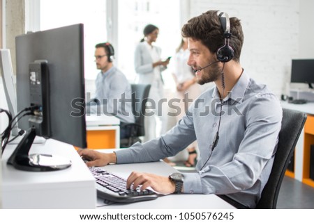 Smiling handsome customer support operator agent with hands-free device working in call center Royalty-Free Stock Photo #1050576245