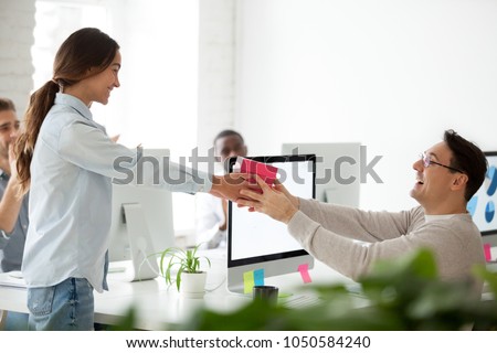 Friendly business team congratulating colleague making surprise present, smiling woman giving excited coworker or boss gift box, employees group greeting man wishing happy birthday in office concept