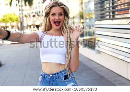 Young stylish woman making selfie on the street, smiling and screaming, surprised emotions, unusual dreads hairstyle, traveling alone in LA