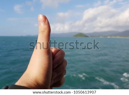 Photo of palm with finger up and sea coast, cloudy sky