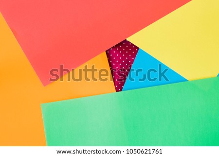Closeup to blue, red, yellow, green and orange sheets of paper put on a creased red paper on white spots. Background.