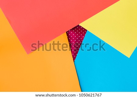 Blue, red, yellow and orange sheets of paper put on a creased red paper on white spots. Background.