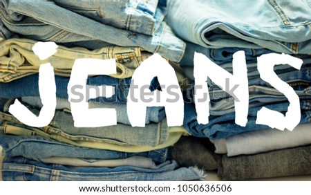 word jeans white on the background of a stack of multi-colored jeans