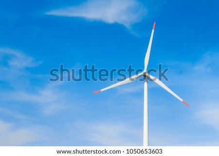 Rotating windmill generating renewable energy with wind power. Sustainability by windmills turbines preventing climate change with regenerative clean green nature energy. Windy blue sky with clouds