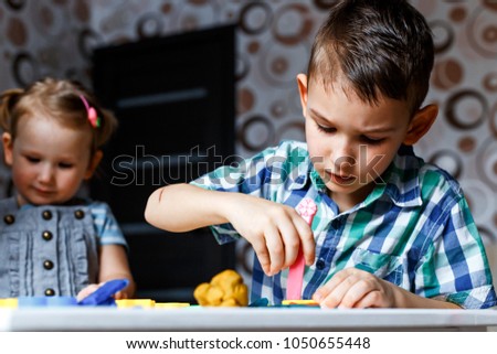 Picture of a sister and a brother playing with color play dough and cutters. Having fun with colorful modeling clay. Creative kids molding at home. Children play with plasticine or dough.