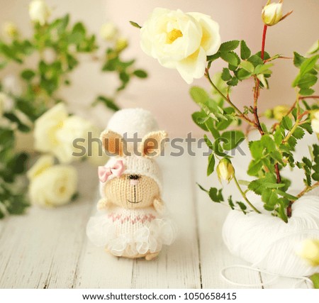 Handmade knitted toy.  Easter Bunny in white dress and hat with pompom among white roses.