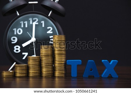 Time to pay TAX concept. TAX alphabet with stack of coin and vintage alarm clock in dark background, business and financial concept idea.