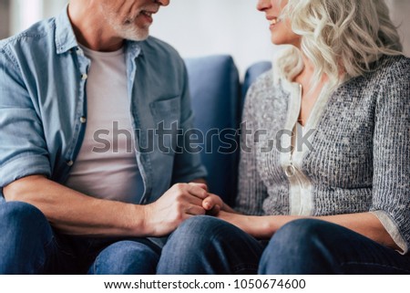 Love lives forever! Cropped image of senior couple at home. Handsome old man and attractive old woman are spending time together. Sitting on a sofa, hugging and holding hands. Royalty-Free Stock Photo #1050674600